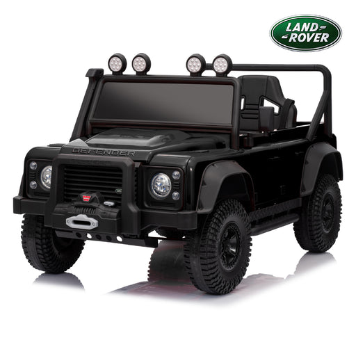A black 4-wheel electric ride-on toy vehicle designed to look like a Land Rover Defender, shown from a three-quarter front angle on a white background with a reflection. A green Land Rover logo badge is visible in the top right corner.