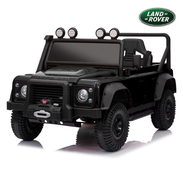 A black 4-wheel electric ride-on toy vehicle designed to look like a Land Rover Defender, shown from a three-quarter front angle on a white background with a reflection. A green Land Rover logo badge is visible in the top right corner.