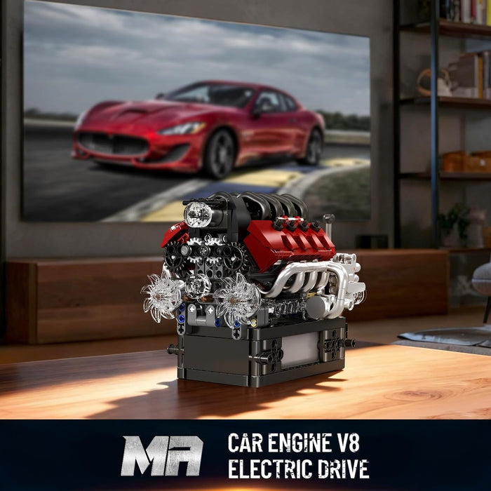 Model car engine V8 with electric drive on a wooden surface, TV screen displaying a red car in the background.