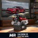 Model car engine V8 with electric drive on a wooden surface, TV screen displaying a red car in the background.